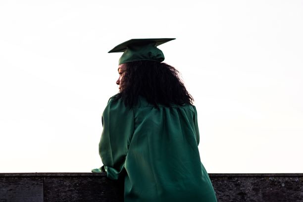 Girl poses in green graduation robe and cap.