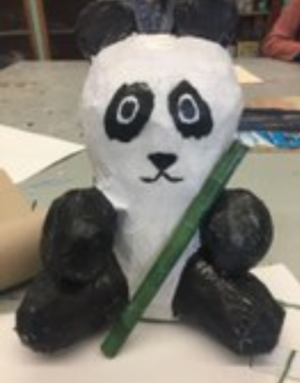 A panda made from a soda bottle, foam balls, paper mache, and a magazine.